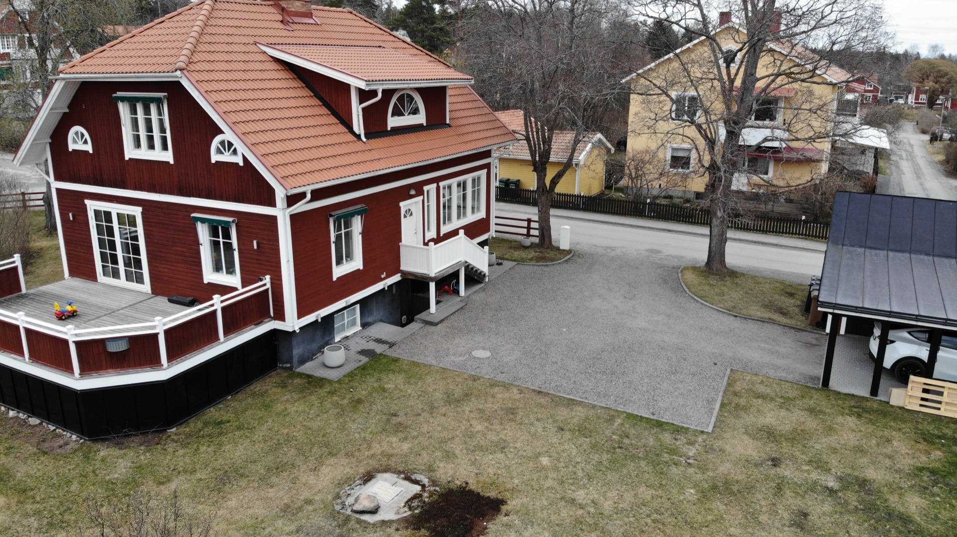 Huset i dag, fotograferat med drönare i mars: rött trähus, liten altan och grusad uppfart